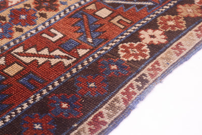 A close-up of an authentic Caucasian  geometric Kuba region antique Karagashli rug with red, blue, beige, and brown woven motifs, shown on a plain white background.
