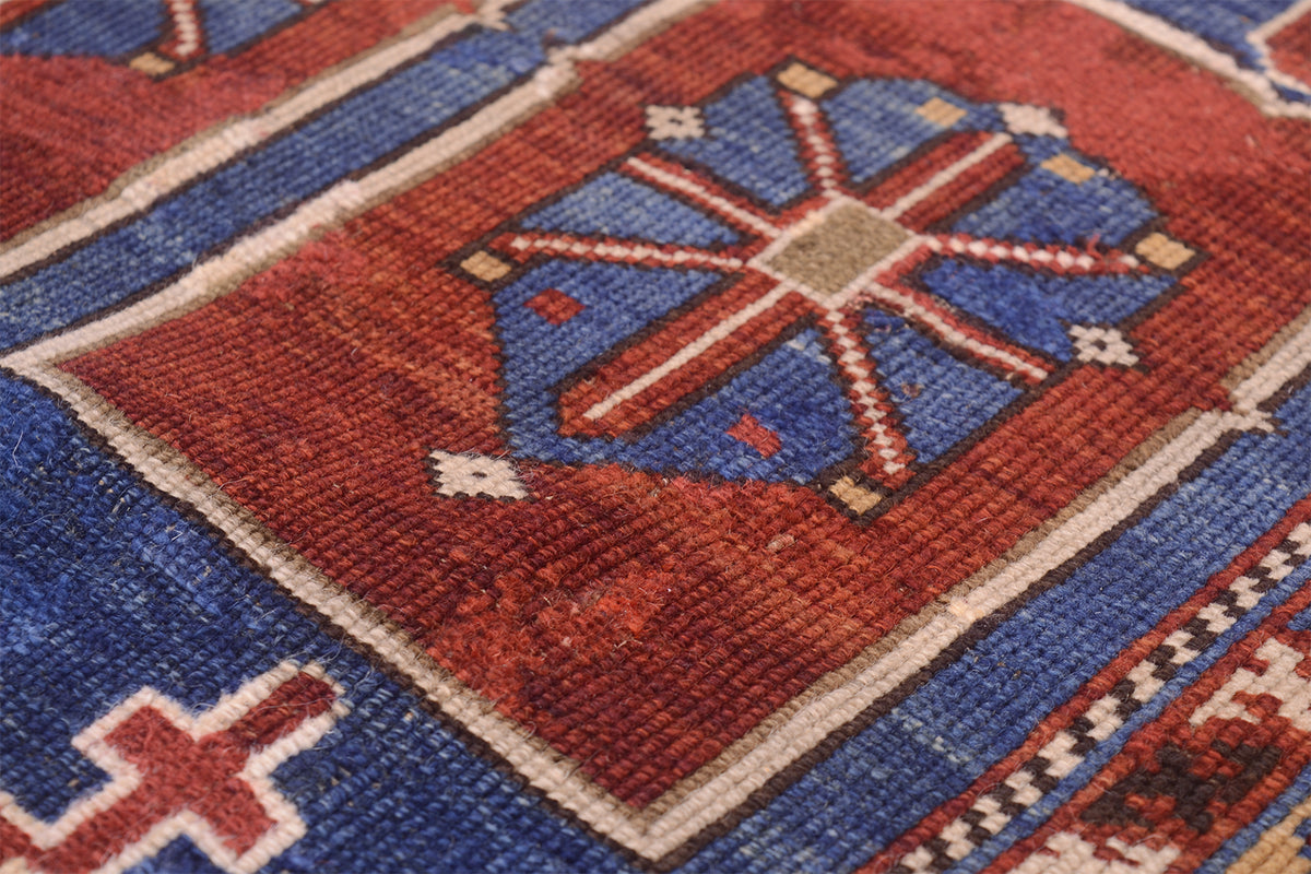 Close-up of a handwoven antique Karagashli rug showing a red and blue geometric pattern with cream borders and a central star-like motif.