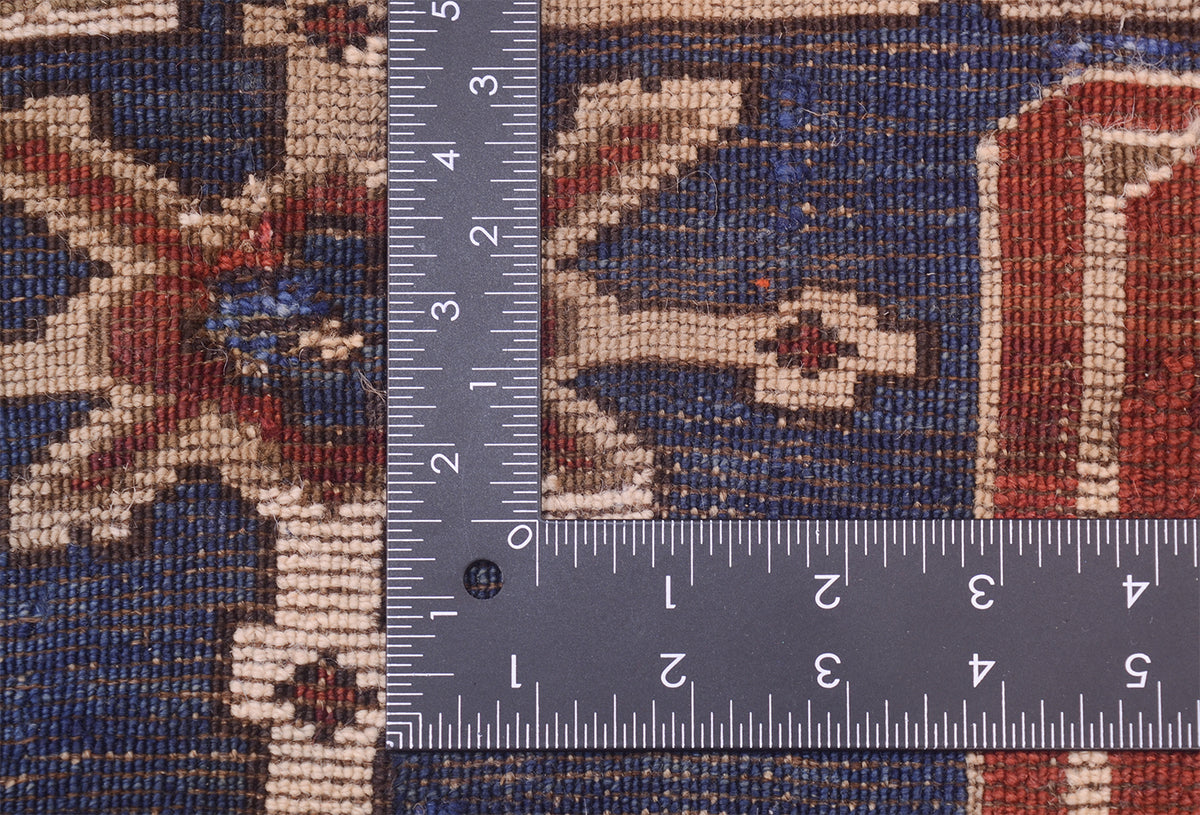 Close-up of the hand-knotted weaver of an antique Caucasian Karagashli rug with a dark blue base, cream motifs, and red accents, shown with metal ruler to show scale of the knotting.