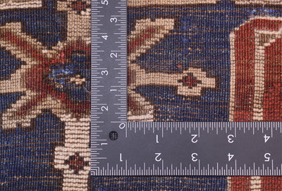 Close-up of the hand-knotted weaver of an antique Caucasian Karagashli rug with a dark blue base, cream motifs, and red accents, shown with metal ruler to show scale of the knotting.