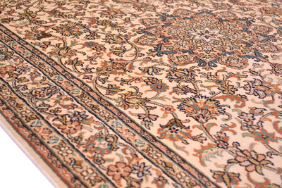 A close-up of an ornate silk area rug with a cream background and intricate floral motifs in navy blue, rust orange, and olive green, showing the detailed woven texture and corner border.