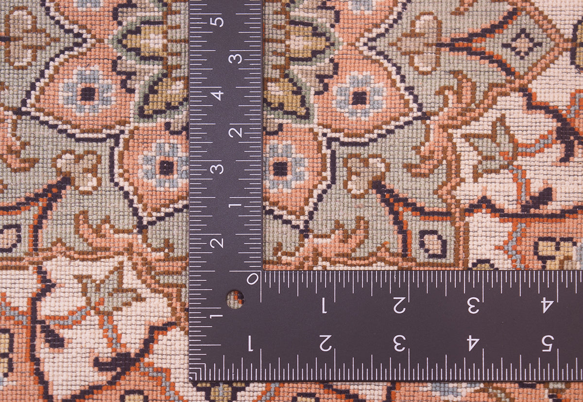 Close-up of the back of a silk Kashmir rug with a  L-shaped ruler placed over it to show scale, featuring a beige, peach, and navy ornamental floral design.