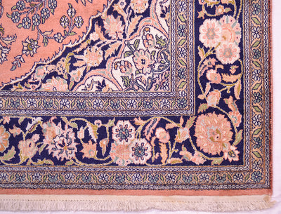 Close-up of an ornate silk Kashmir area rugs corner showing a navy blue border with peach, cream, and green botanical motifs and a fringed edge.