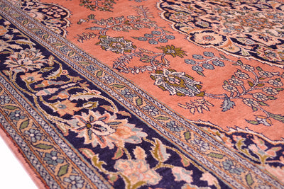 A close-up of an ornate pattern silk Kashmir rug with a pink field, dark navy borders, and floral motifs in beige, green, and blue.