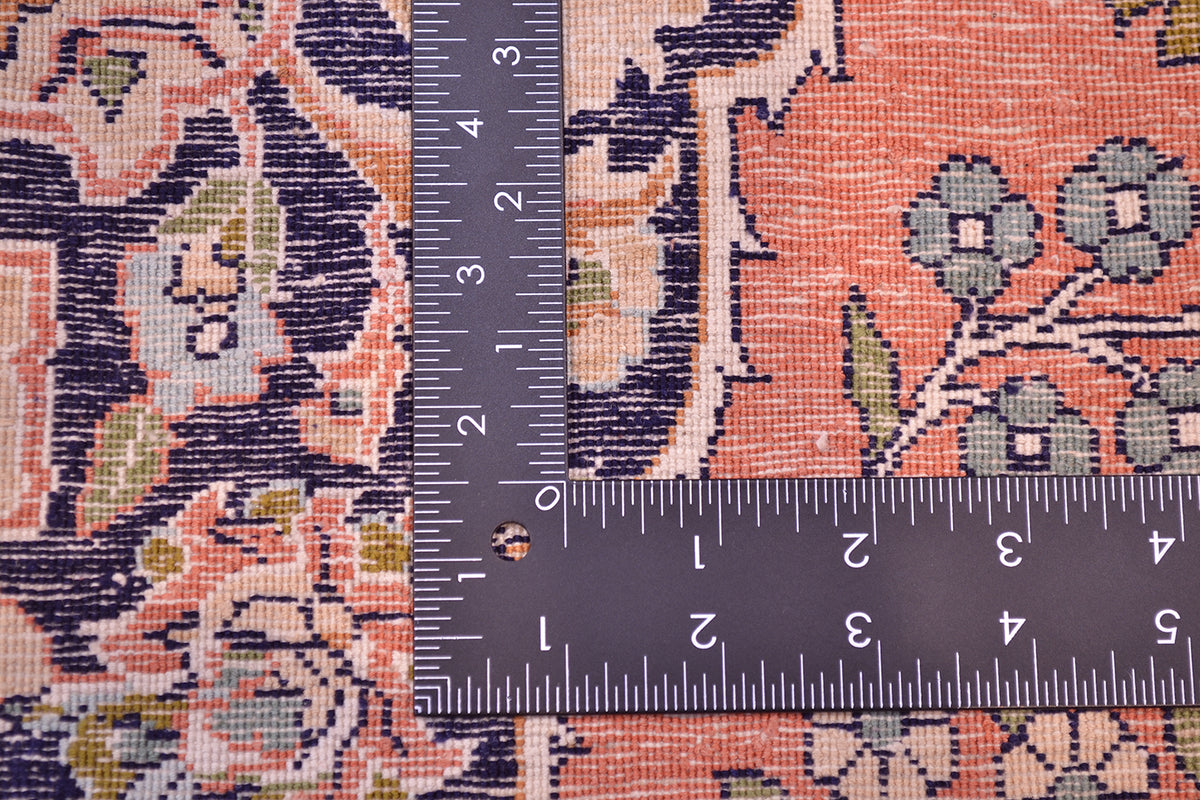 Close-up of a second hand silk Kashmir rug with a dark ruler placed  to show scale, featuring pink, navy, beige, and muted green floral motifs.
