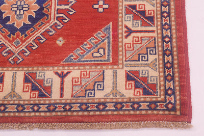 Close-up of red Kazak rug corner with blue geometric panel and border trim