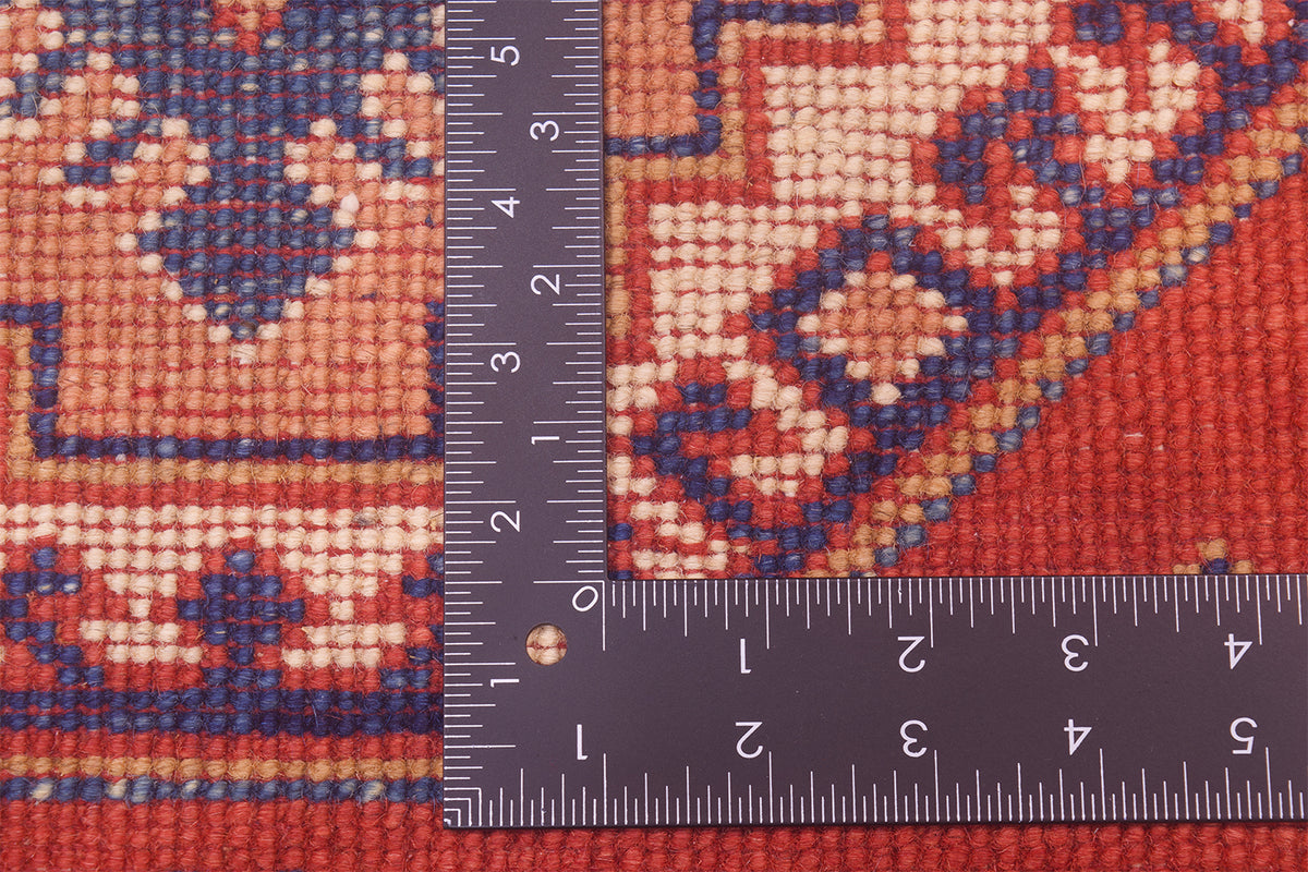Red Kazak rug fabric close-up with measuring tape over woven texture