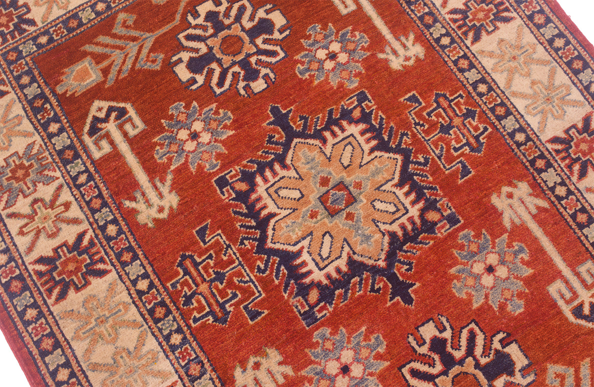 Kazak rug close-up: rust-red field with central rosette and navy geometric outlines