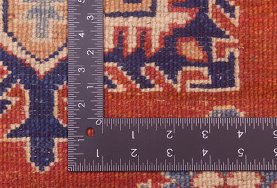 Kazak rug close-up with ruler scale showing dense weave on rust-red fabric
