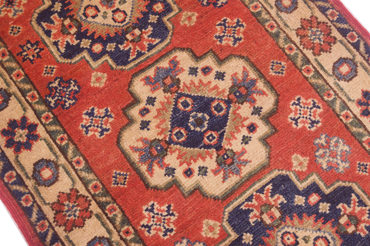 A close-up of a traditional small size handmade Kazak Mat with a red field, beige borders, and navy blue medallions and floral motifs.