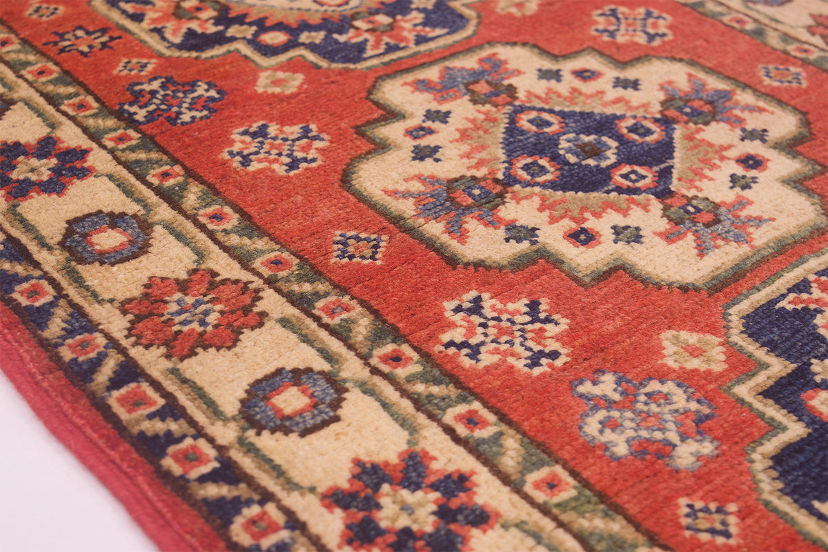 A close-up of a traditional patterned area rug with a red field, beige borders, and navy blue floral medallions.