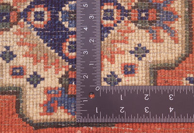 Close-up of the knotted back of ornate small size handmade Kazak Mat with a dark metal L-square ruler and measuring tape placed over it to show scale, showing the rug's cream, rust red, and navy blue woven design.
