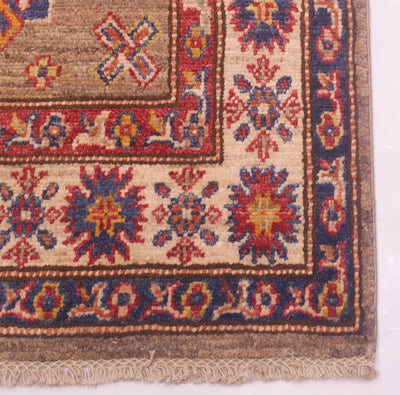 A close-up of an extra long handmade Afghan Kazak runner corner showing a beige field with red, navy, and yellow floral motifs and a fringed edge.