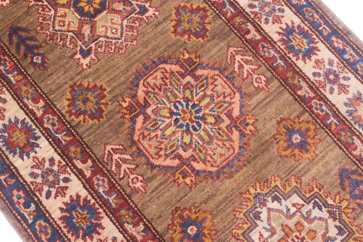 A close-up of a traditional handwoven Afghan Kazak long runner with a brown field, featuring a central medallion and geometric borders in beige, blue, red, and orange.