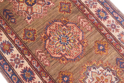 A close-up of a traditional handwoven Afghan Kazak long runner with a brown field, featuring a central medallion and geometric borders in beige, blue, red, and orange.