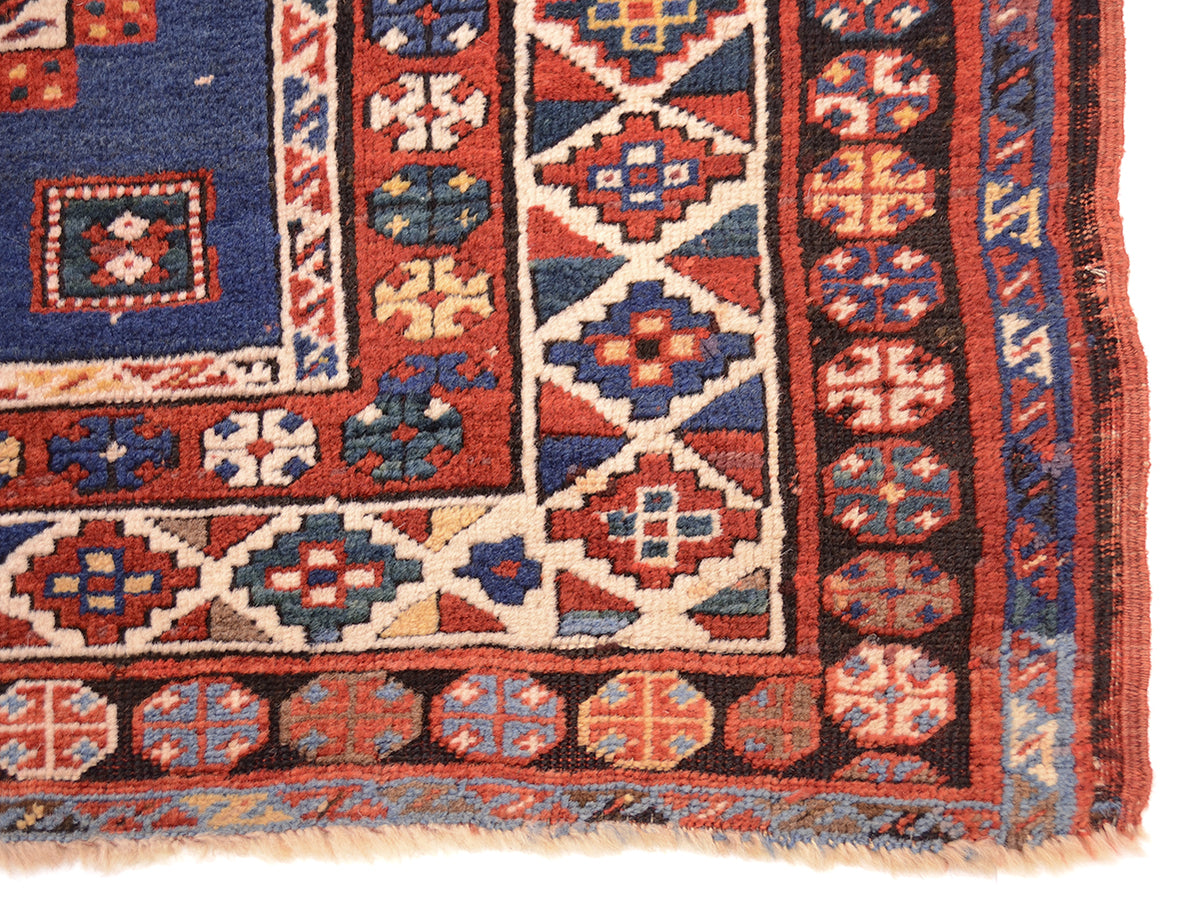 Corner of antique kazak rug showing pure woolwarp fringe and black corrosion in outer border background.