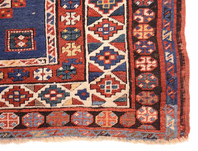 Corner of antique kazak rug showing pure woolwarp fringe and black corrosion in outer border background.