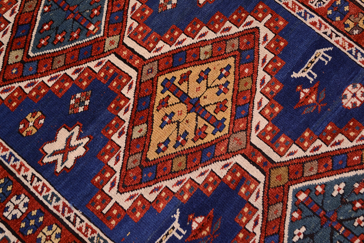 Close up detail of main field of Antique kazak handknotted rug with stepped medallions with blues, yellow golds, nut browns and natural white for contrast.  Star flower centre design of the diamond medallions.