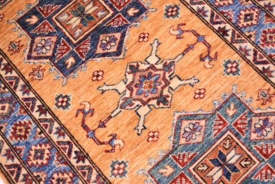 A close-up of a traditional handwoven small fine Afghan Kazak rug with a warm amber yellow field, featuring a central starburst medallion and geometric borders in navy blue, rust red, and cream.