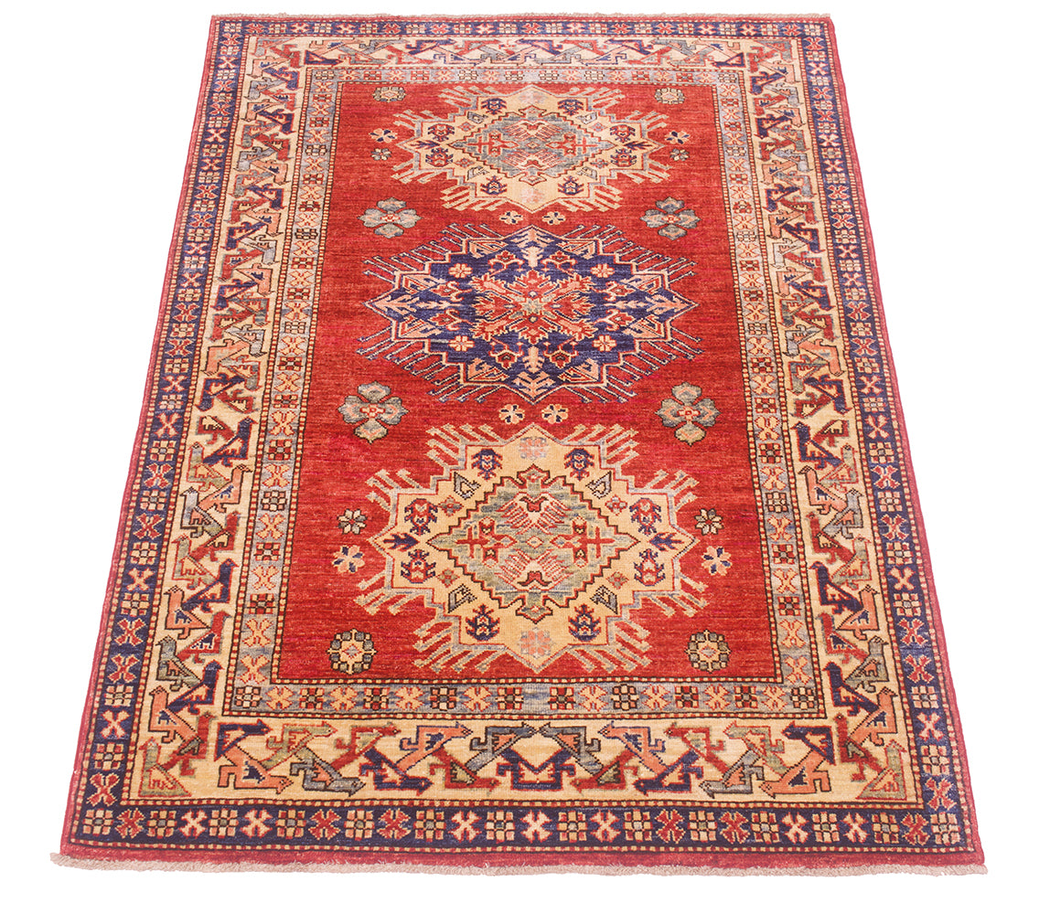 A rectangular traditional oriental Afghan Kazak design rug with a vibrant rust-red field, featuring two large central medallions in blue, beige, and red, surrounded by a detailed geometric border.