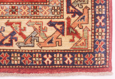 A close-up of a patterned Kazak rug corner showing a cream main border with red, navy, and grey geometric motifs and a red edge.