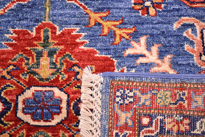 Close-up of the weave underside of a Handmade Fine Kazak wool Rug showing a blue field with red, beige, and green floral motifs, plus cream fringe and part of the border.