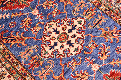 A close-up of a handmade Fine Kazak wool Rug with a blue field, cream central medallion, and orange, red, and green floral motifs.