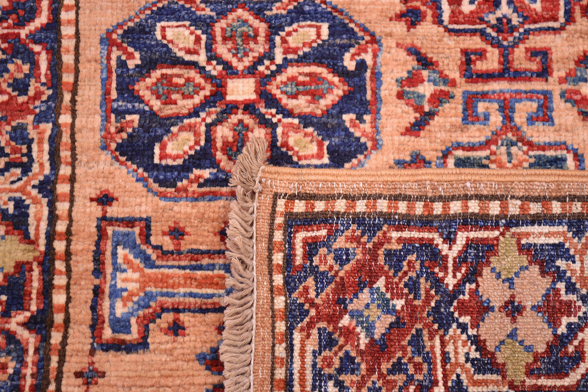 Close-up of the hand-knotted back of a Fine Kazak Peach colour Handmade runner corner showing a peach base with navy, rust red, and beige geometric and floral motifs, plus a short beige fringe along one edge.