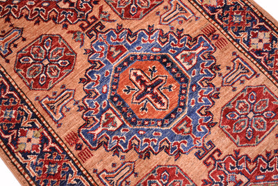 A close-up of a traditional patterned Kazak runner with a central medallion, featuring red, blue, and orange motifs on a warm peach background.
