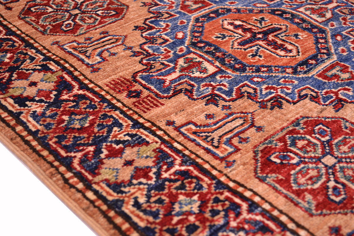A close-up of a traditional patterned fine Kazak handmade runner showing its detailed woven design in peach, red, blue, and beige.