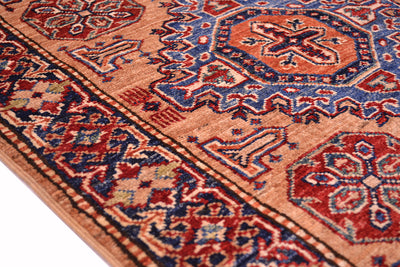 A close-up of a traditional patterned fine Kazak handmade runner showing its detailed woven design in peach, red, blue, and beige.