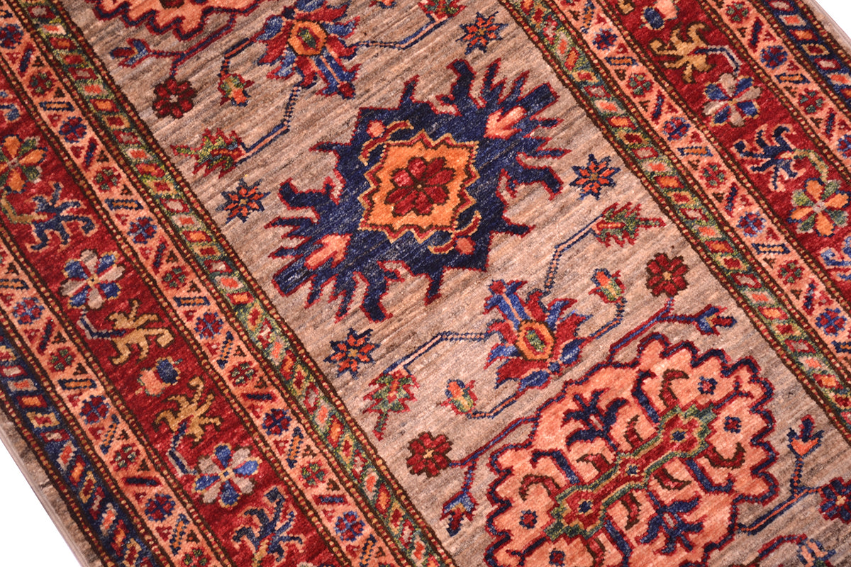 A close-up of a traditional handwoven Kazak Runner rug with a grey centre field, red borders, and blue and orange floral motifs.