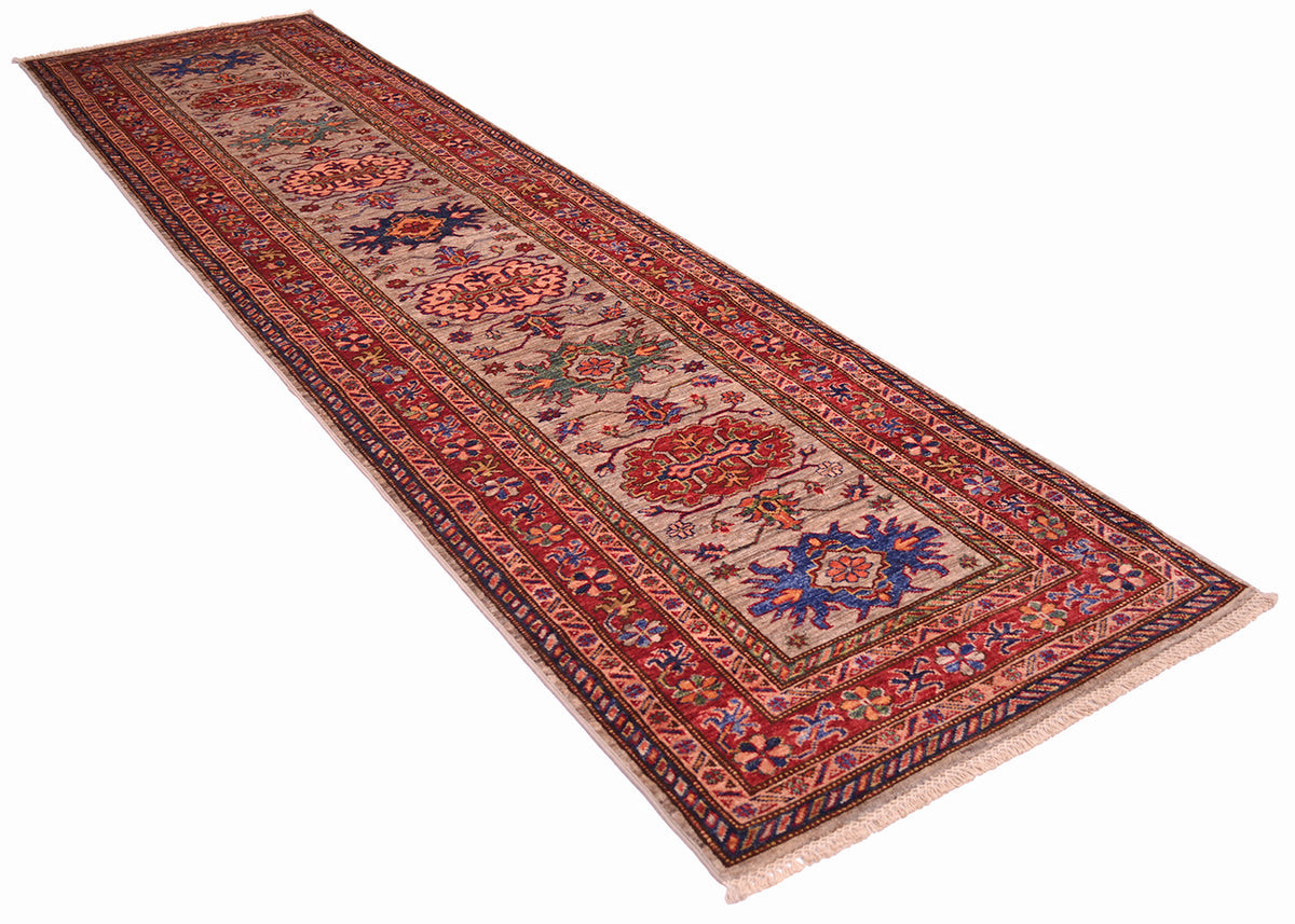 A long rectangular Kazak Runner rug with an intricate traditional pattern in red, blue, green, and grey, shown on a plain white background.