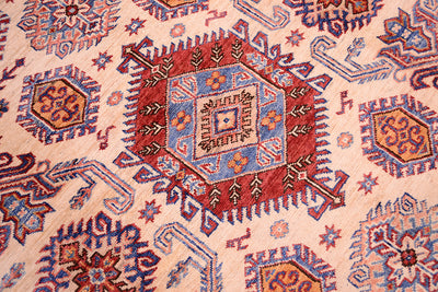 A close-up of a traditional patterned fine handmade Afghan Kazak carpet featuring a central red and blue medallion surrounded by geometric motifs on a light beige background.