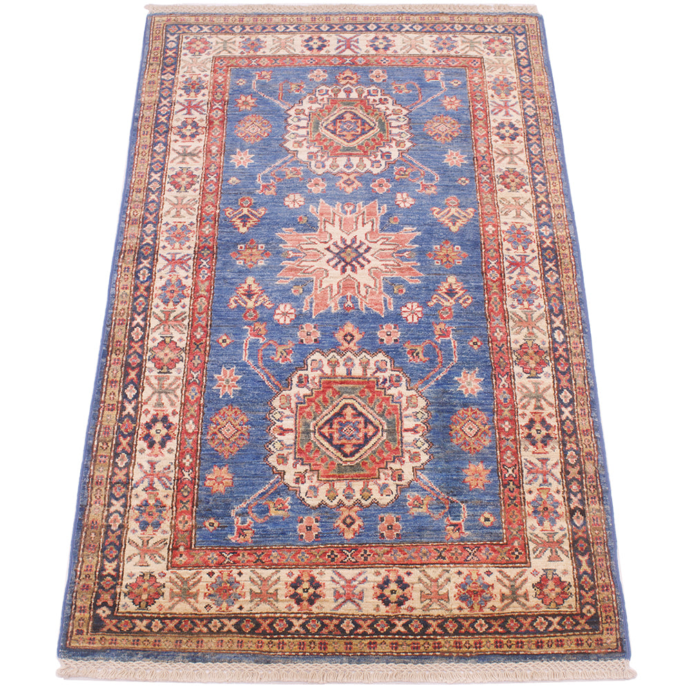 A traditional rectangular blue fine Kazak rug with a blue field, beige borders, and red and cream medallions, shown flat against a white background.