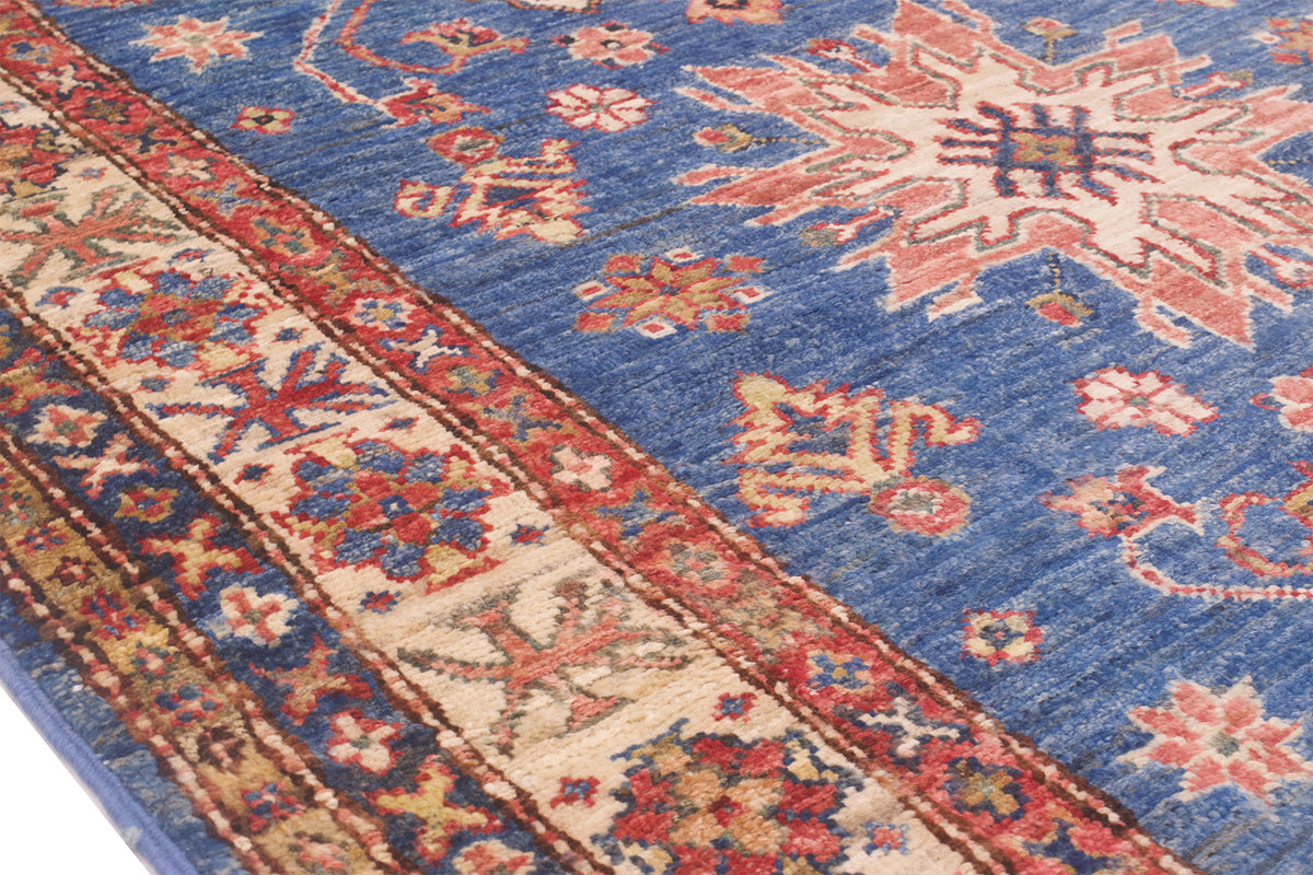 A close-up of a traditional Afghan Kazak patterned rug with a medium blue field, beige borders, and red, orange, and cream motifs.