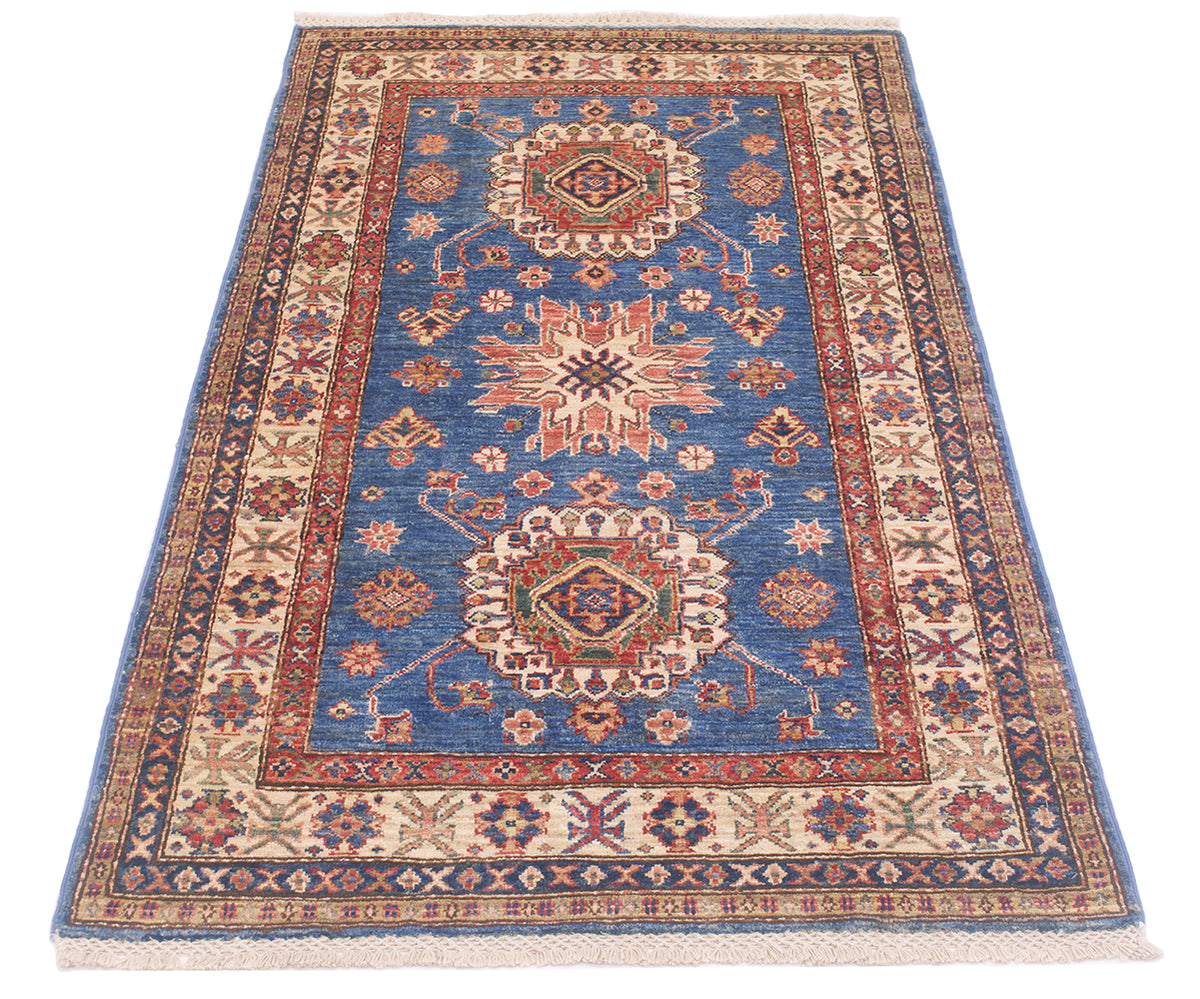 A traditional oriental-style supreme Kazak rug with a blue field, beige and red borders, and central medallions, shown flat against a white background.