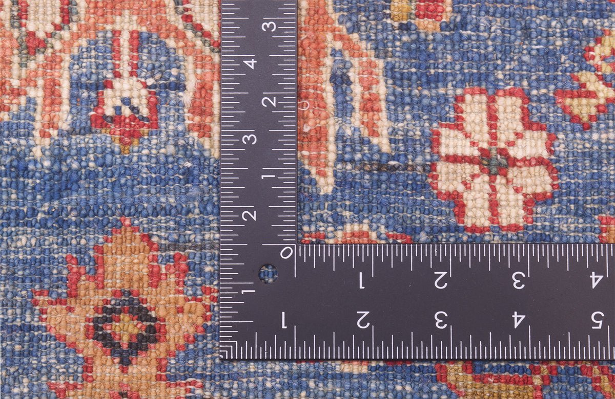 Close-up of the hand-knotted weave of a blue fine Kazak rug with a dark ruler placed on top to show scale of the knot density, featuring a blue base with red, beige, and cream floral motifs.