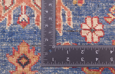 Close-up of the hand-knotted weave of a blue fine Kazak rug with a dark ruler placed on top to show scale of the knot density, featuring a blue base with red, beige, and cream floral motifs.