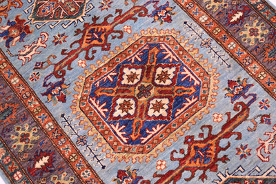 A close-up of a traditional patterned rug featuring a central medallion with blue, red, beige, and orange motifs on a light blue field.