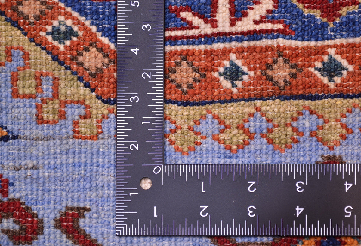 Close-up of the fine light blue Afghan Kazak rug with a dark metal ruler placed along the edge to show the scale of the weave and design.