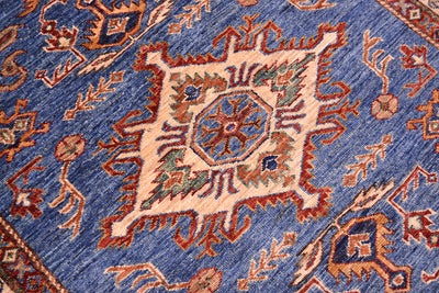 A close-up of a traditional Handmade Fine Kazak Rug with blue featuring a central medallion in beige, blue, rust orange, and green on a blue field.