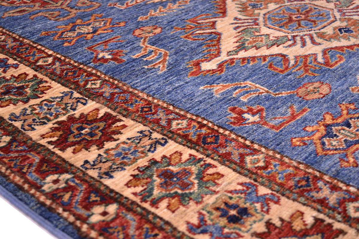 A close-up of a traditional patterned Handmade Fine Kazak Rug with blue field, beige borders, and red, orange, and green woven motifs.
