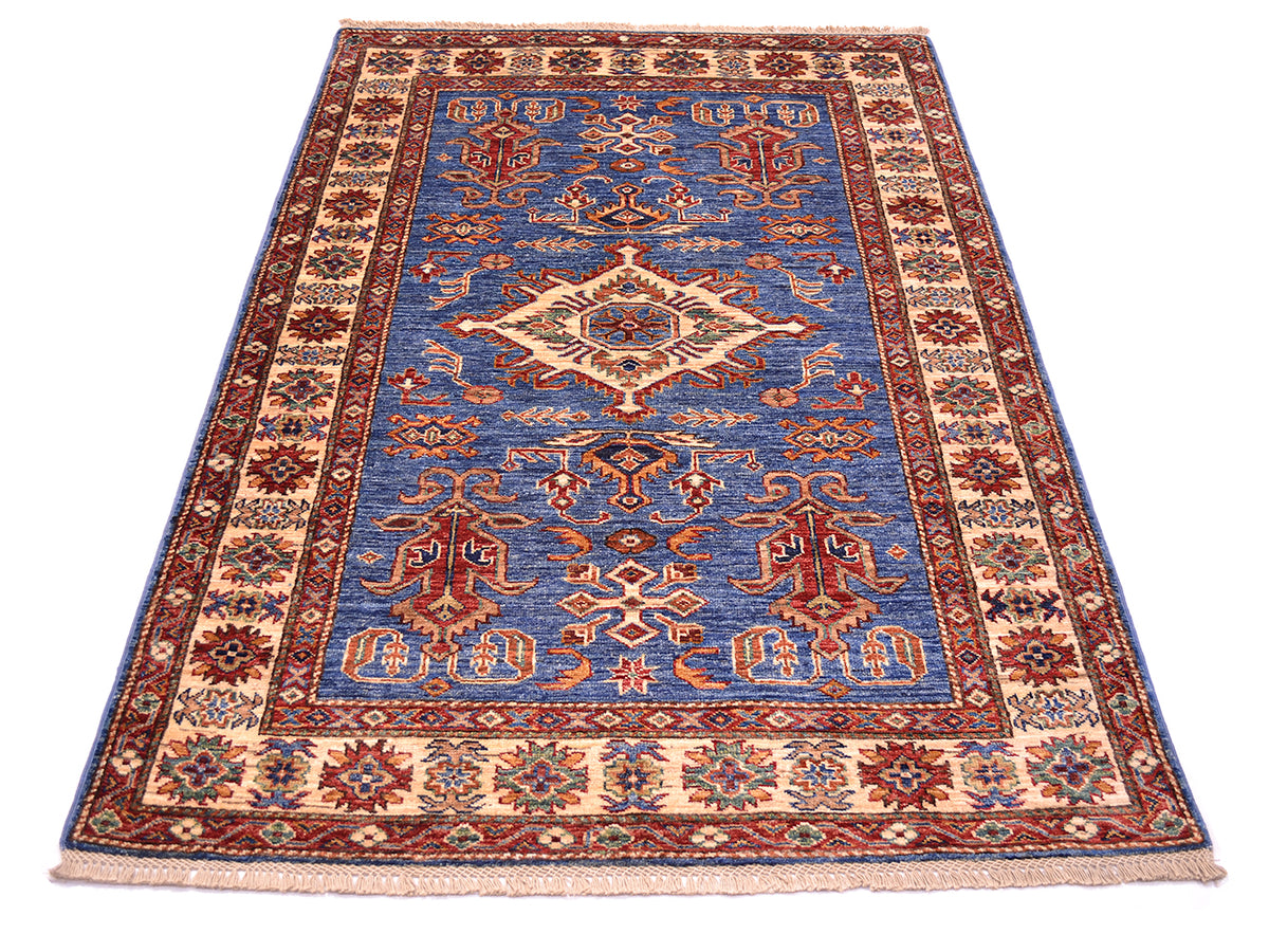A traditional Kazak style area rug with a blue center field, beige and red borders, and intricate floral motifs, shown flat against a white background.