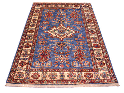 A traditional Kazak style area rug with a blue center field, beige and red borders, and intricate floral motifs, shown flat against a white background.