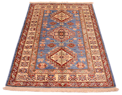 A traditional hand-knotted wool Afghan Fine Kazak Small rug with a geometric pattern, featuring a blue centre field, beige borders, and rust-red accents, shown flat against a white background.