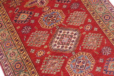 A close-up of a Fine red handmade Afghan Kazak Rug with a dominant red field, featuring geometric medallions and floral motifs in beige, blue, green, and orange.
