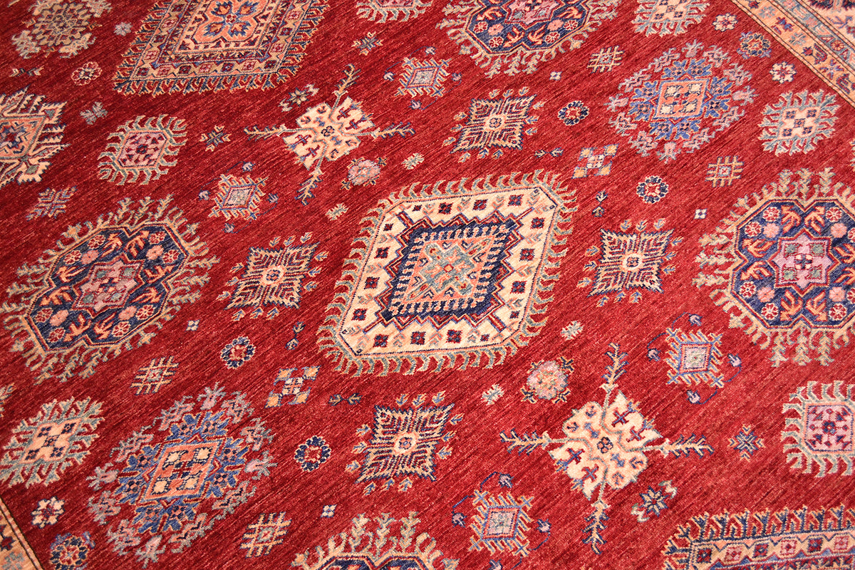 A close-up of a large red Kazak carpet with traditional medallions and floral motifs in beige, blue, and cream.
