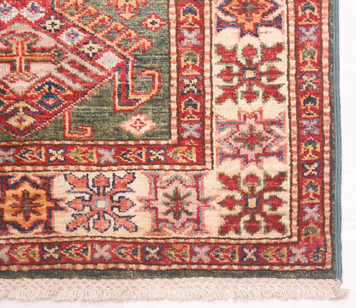 A close-up of a traditional patterned Afghan runner corner showing cream, red, green, and blue geometric motifs with a fringed edge.