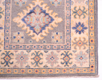 A close-up of a traditional patterned Afghan Yakash runner corner showing a central diamond medallion, floral motifs, and a grey-blue field with cream, blue, and orange accents.